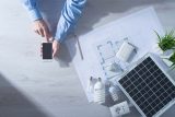 A pair of male hands holding a cell phone with sustainable energy solutions like solar panels and energy efficient spiral bulbs