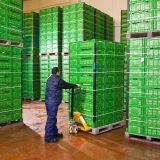 A worker in blue moves pallets of green crates in cold storage