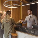 A male front desk worker at a hospitality resort that has benefitted from eaas assists two female patrons as they check in.