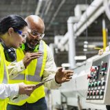 A male and female both in bright yellow safety vests and safety flasses examine the settings on a piece of manufacturing equipment while conducting an industrial energy audit with Ionic Blue LLC